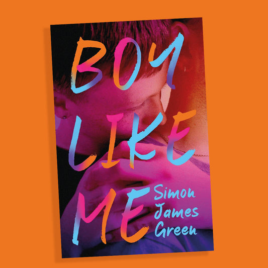The paperback book Boy Like Me sits on an orange background. The book cover has a teen boy holding the shoulder of another boy, lovingly.