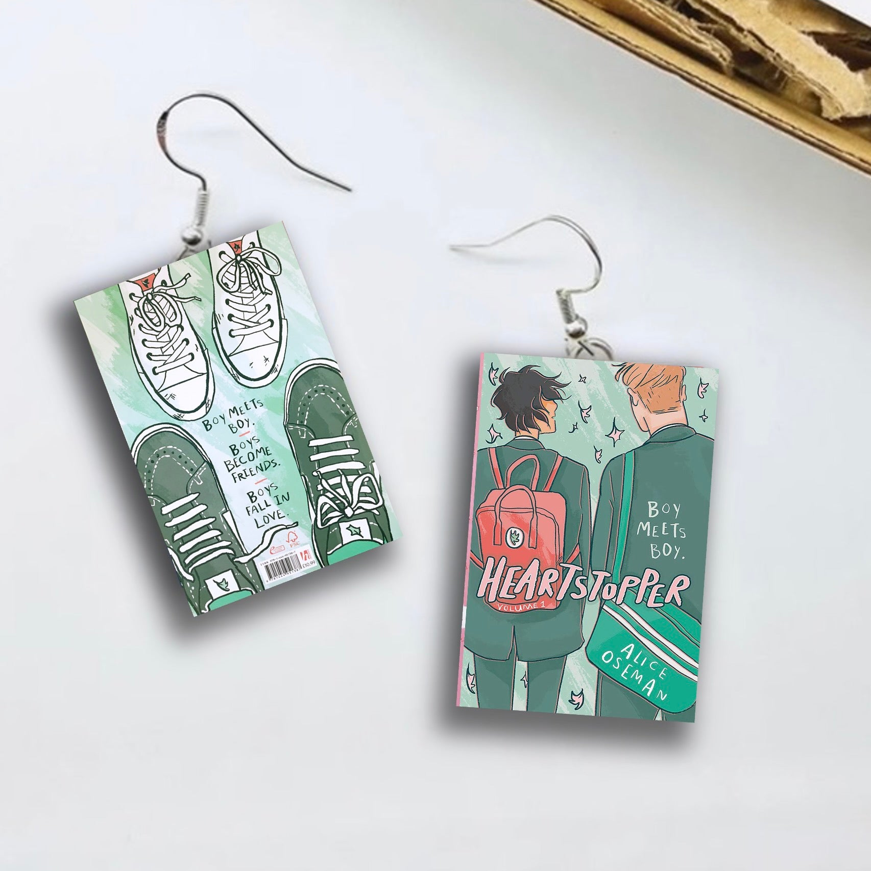 A pair of earrings that are the book cover of Heartstopper volume 1. 