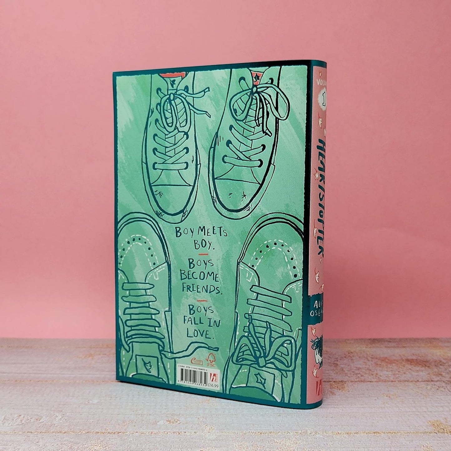 A special shiny green back cover of Heartstopper Volume One. The image is a birds eye view of two pairs of shoes -  a pair of sneakers and vans.