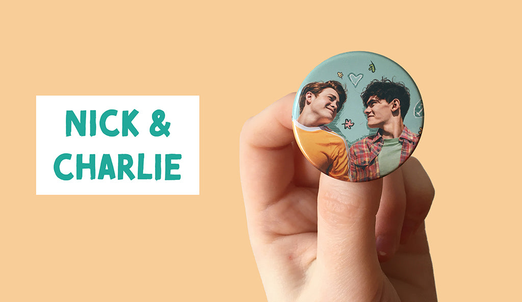 A Heartstopper badge showing Nick and Charlie (two white teens) smile at one another as they lie on their backs. Some doodled leaves and a heart decorates the space between them. 